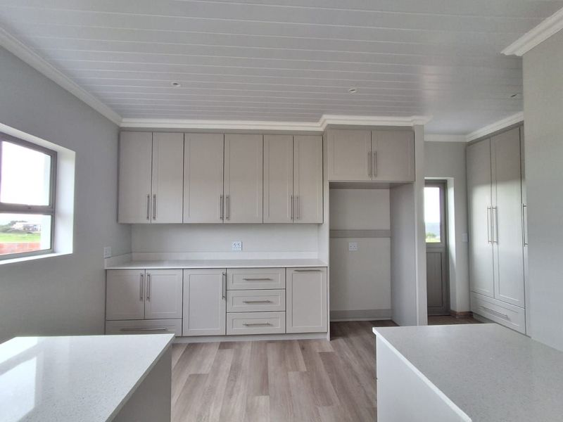 A modern, clean kitchen featuring neutral cabinetry, stone countertops, and light wood-look flooring, offering a bright and functional space.
