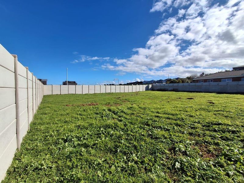 A vacant residential plot featuring a level grassed area enclosed by a precast concrete boundary wall.