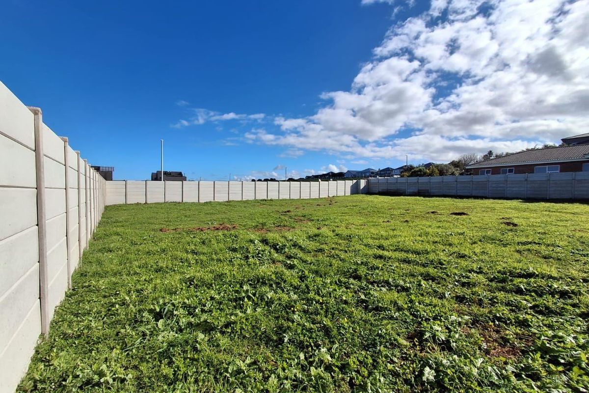 A vacant residential plot featuring a level grassed area enclosed by a precast concrete boundary wall.