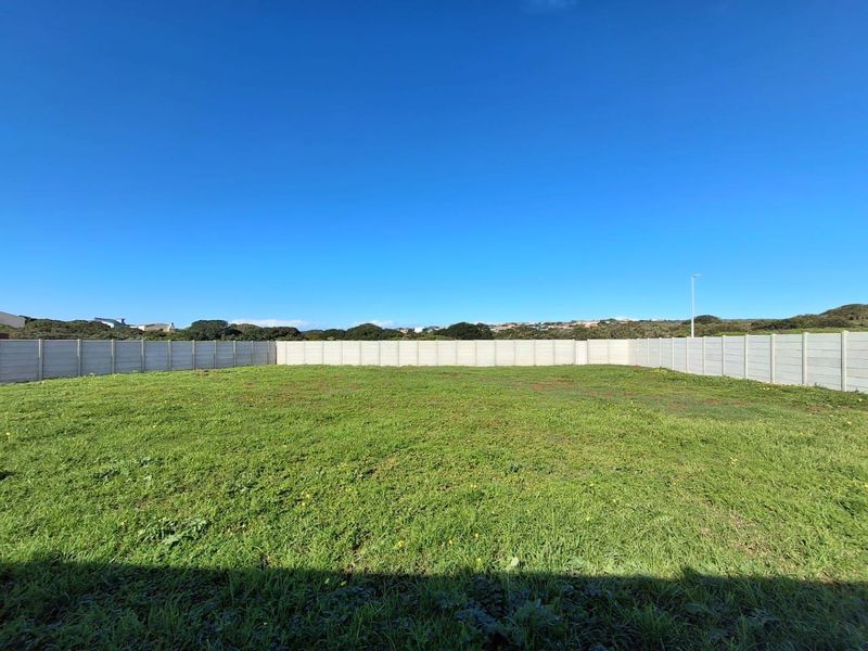 A level, grassed vacant residential plot enclosed by a precast concrete boundary wall.