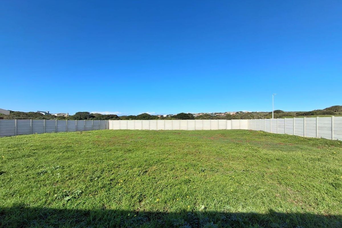 A level, grassed vacant residential plot enclosed by a precast concrete boundary wall.