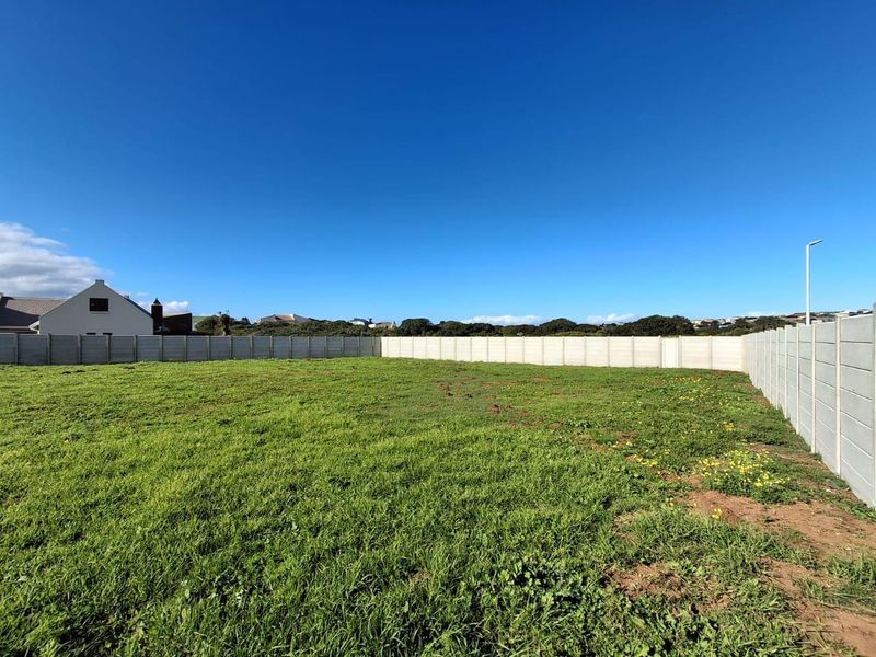 A vacant residential plot featuring a level grassed area enclosed by precast concrete boundary walls under a clear blue sky.