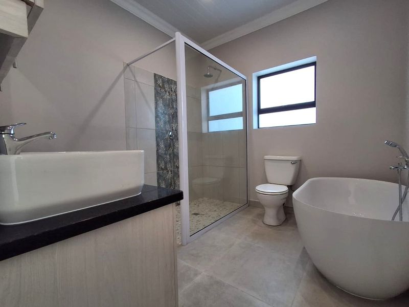 Modern bathroom featuring a sleek freestanding bathtub, a glass-enclosed shower with decorative tiling, a vanity basin, and a toilet.