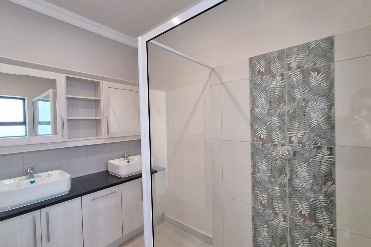 Modern bathroom featuring a double vanity with vessel sinks, built-in cabinetry, and a spacious walk-in shower with decorative feature tiling.