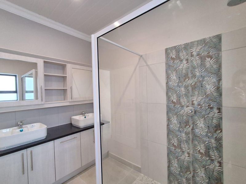 Modern bathroom featuring a double vanity with vessel sinks, built-in cabinetry, and a spacious walk-in shower with decorative feature tiling.