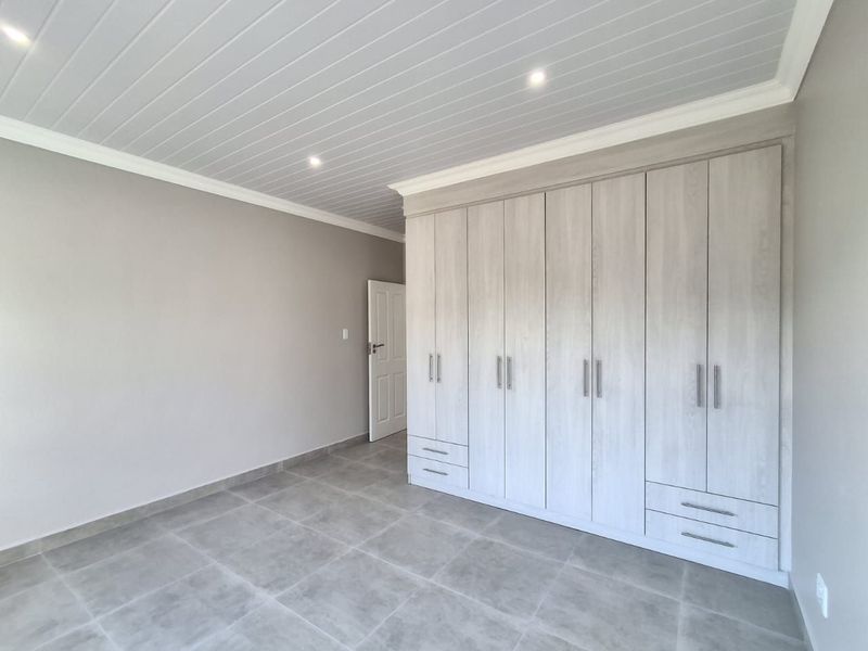 A bright, modern bedroom featuring neutral grey tiled floors, a tongue and groove ceiling with recessed lighting, and extensive built-in cabinetry.