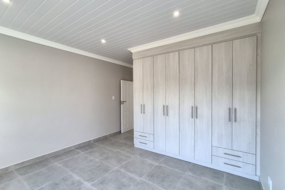 A bright, modern bedroom featuring neutral grey tiled floors, a tongue and groove ceiling with recessed lighting, and extensive built-in cabinetry.