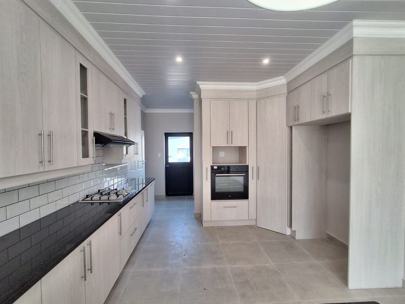 Modern kitchen featuring light wood-finish cabinetry, black granite countertops, subway tile backsplash, built-in oven, gas hob, and tiled flooring.