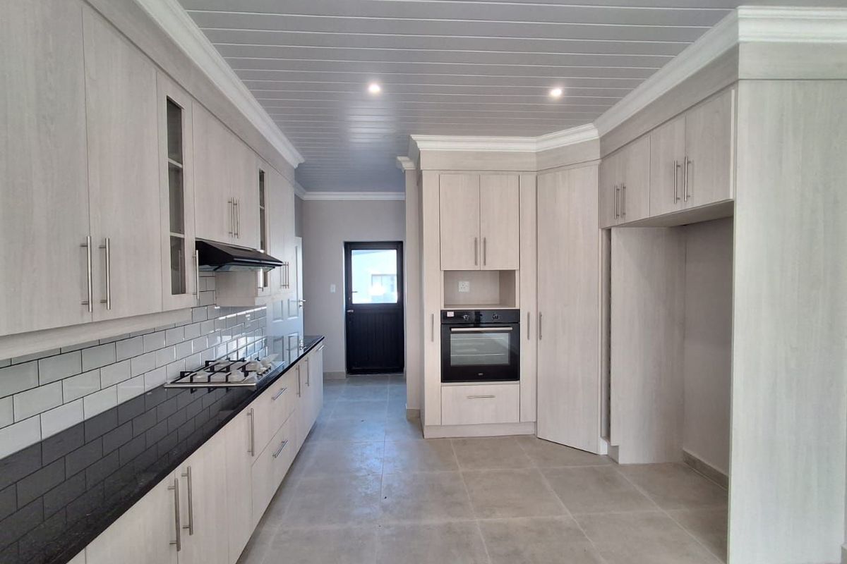 Modern kitchen featuring light wood-finish cabinetry, black granite countertops, subway tile backsplash, built-in oven, gas hob, and tiled flooring.