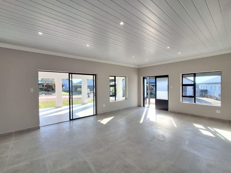 A bright and spacious open-plan living area featuring modern tiled floors, a clean tongue and groove ceiling with recessed lighting, and large sliding glass doors.