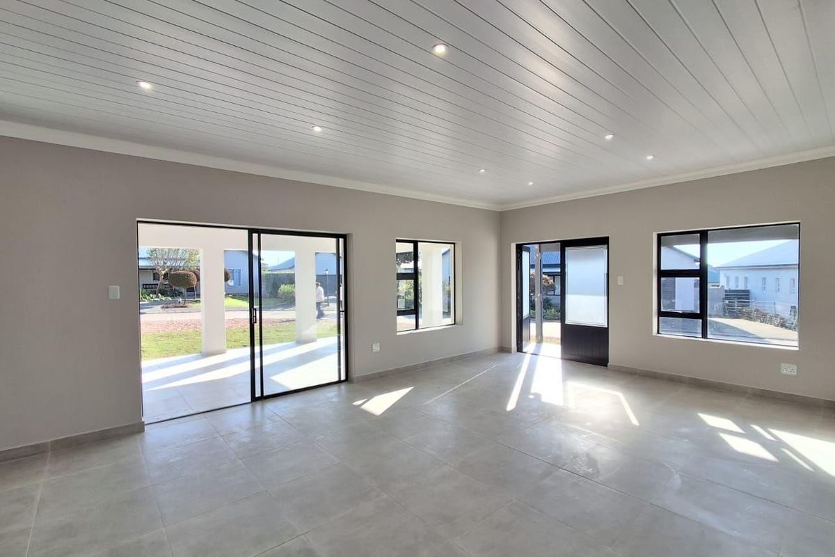 A bright and spacious open-plan living area featuring modern tiled floors, a clean tongue and groove ceiling with recessed lighting, and large sliding glass doors.