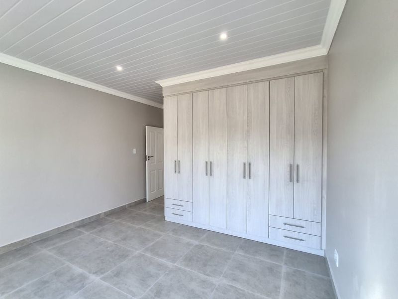 A bright, modern bedroom featuring neutral tiled flooring, a tongue and groove ceiling with recessed lighting, and extensive built-in cabinetry.