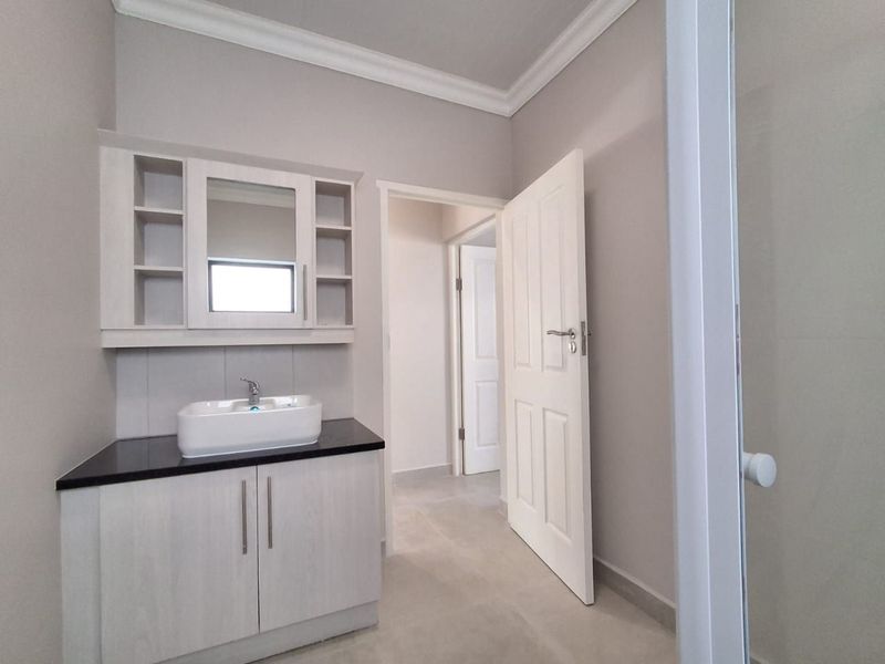 A clean, modern bathroom featuring a vanity with a vessel sink, built-in shelving, and neutral tiled flooring.