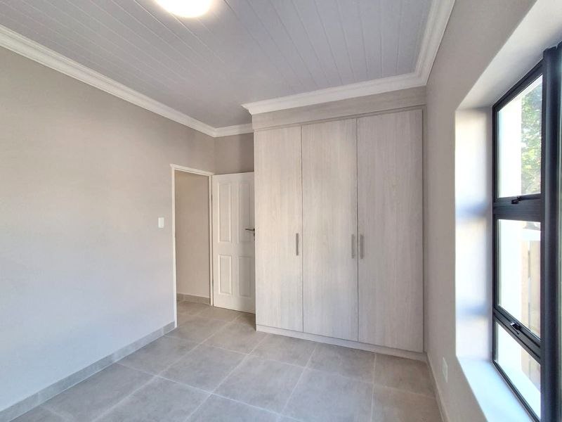 A bright, modern bedroom featuring neutral tiled flooring, a tongue and groove ceiling, and ample built-in cupboard storage.