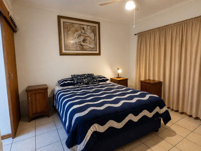 A functional bedroom featuring tiled flooring, a ceiling fan, and a built-in wardrobe, offering a neutral base for personalization.