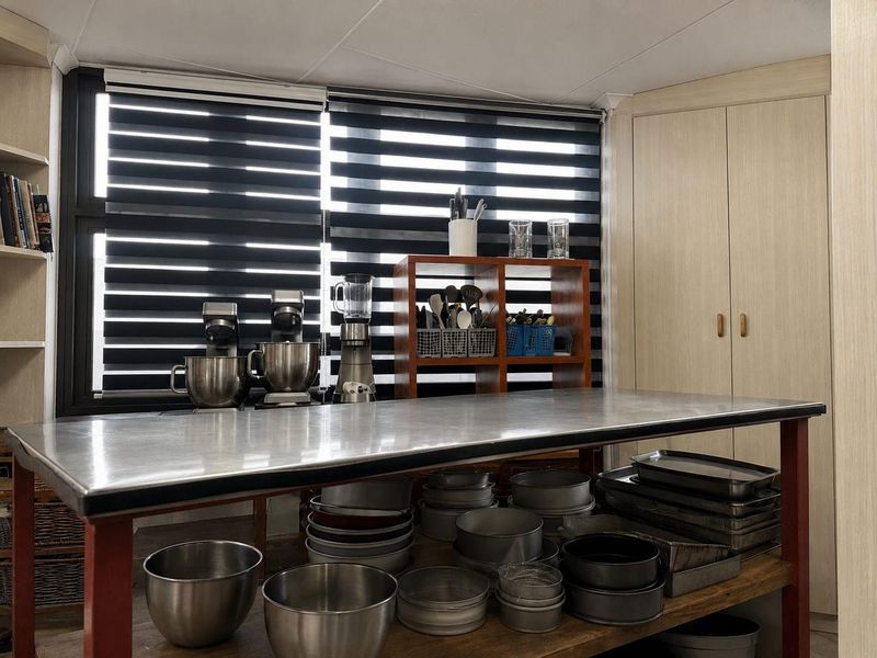 A functional scullery or prep area featuring built-in cabinetry, a large stainless steel work surface, and modern zebra blinds.