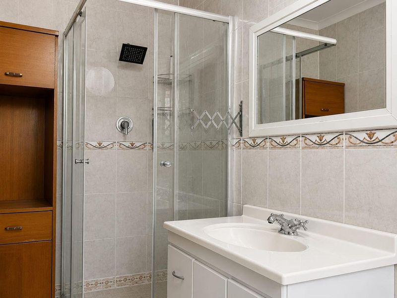 A functional bathroom featuring a glass shower enclosure, a vanity basin with storage, and neutral wall tiling with decorative border accents.