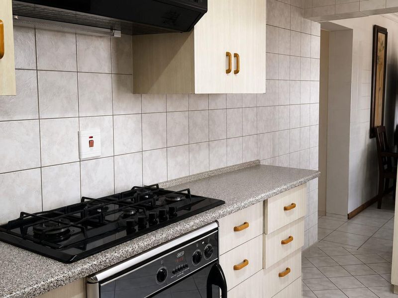 A functional kitchen featuring a gas hob, built-in oven, extractor fan, and neutral cabinetry with tiled splashbacks and flooring.