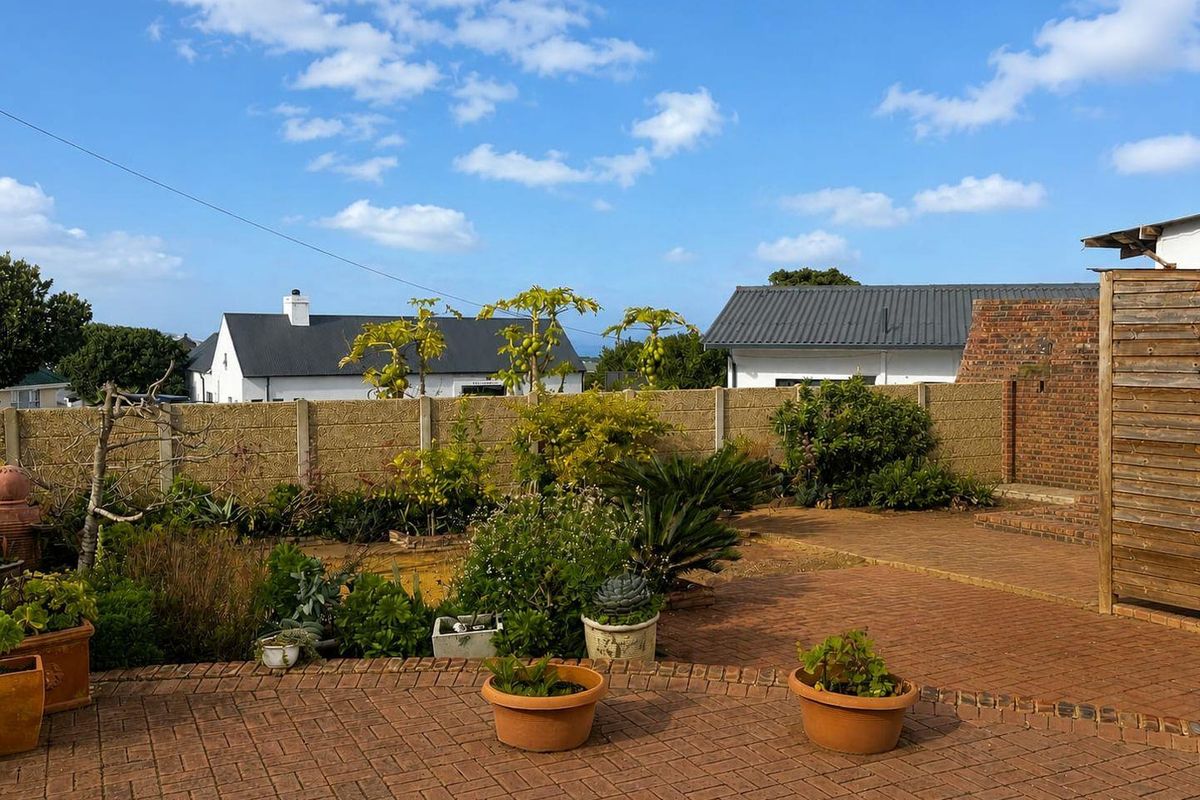 A rear garden area featuring brick paving, a precast concrete boundary wall, and a brick feature wall with a timber privacy screen.