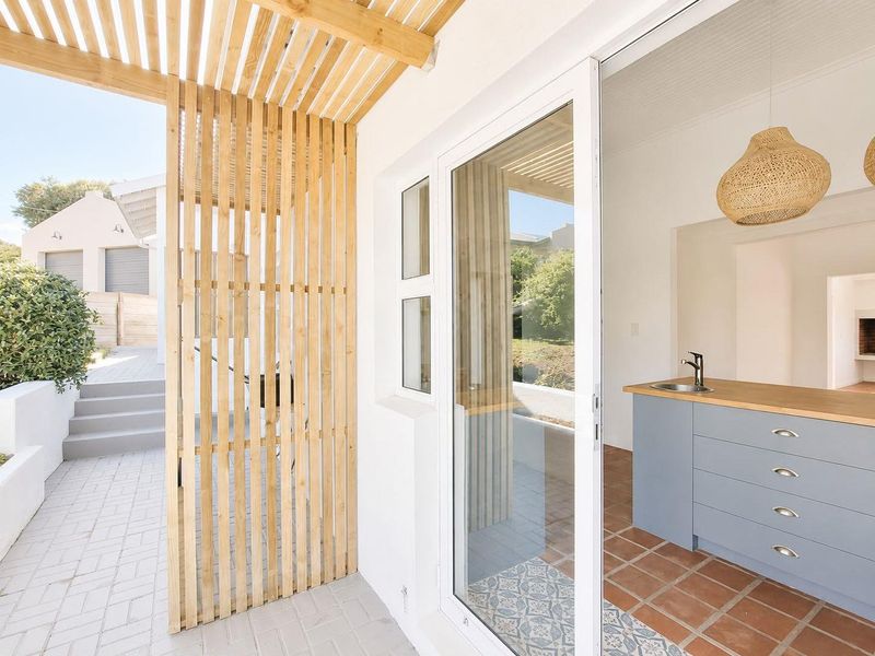 A modern outdoor patio area featuring a timber slat pergola, paved flooring, and a seamless transition to an interior kitchen space with built-in cabinetry.
