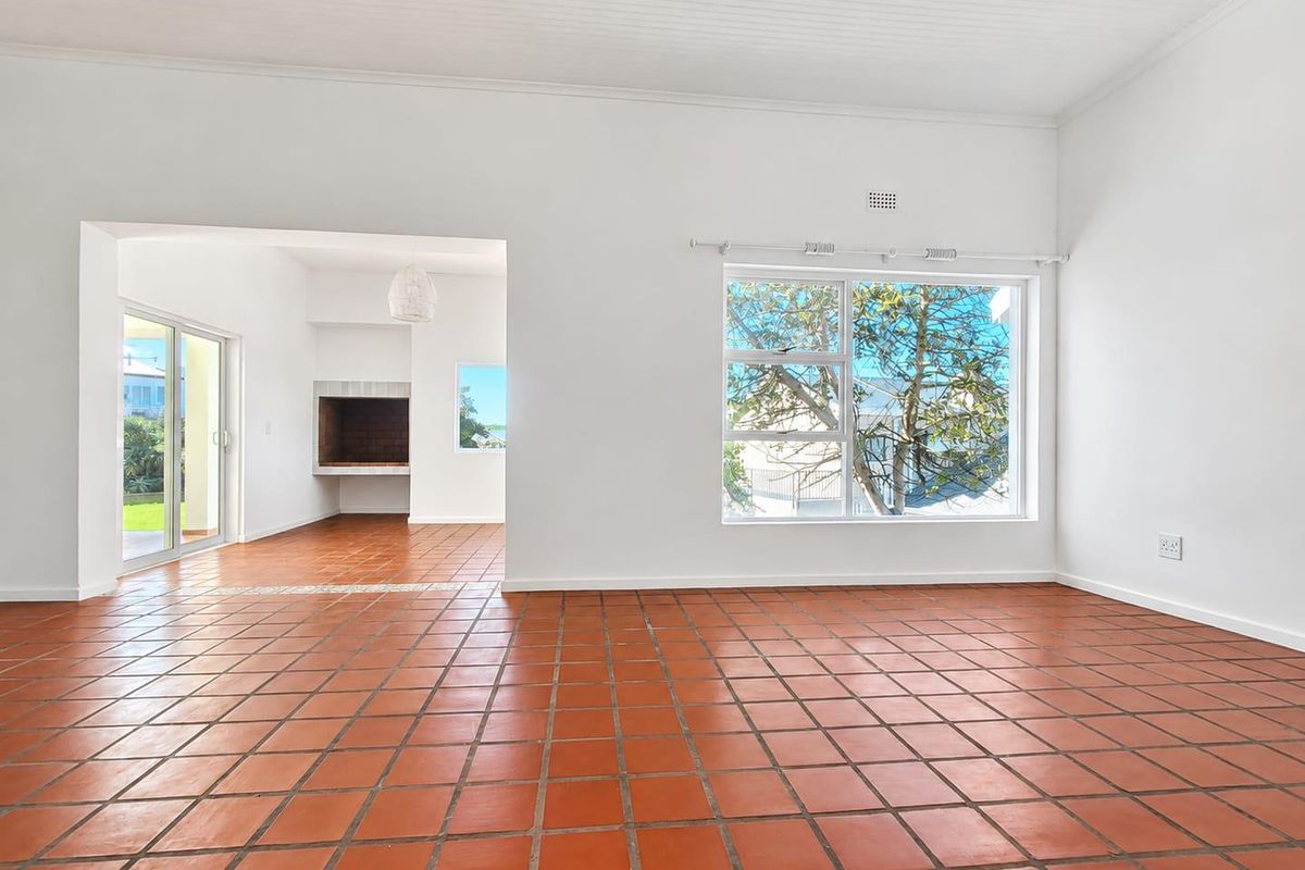Spacious, light-filled living area featuring traditional terracotta tile flooring, a built-in fireplace, and large windows with access to an outdoor patio space.