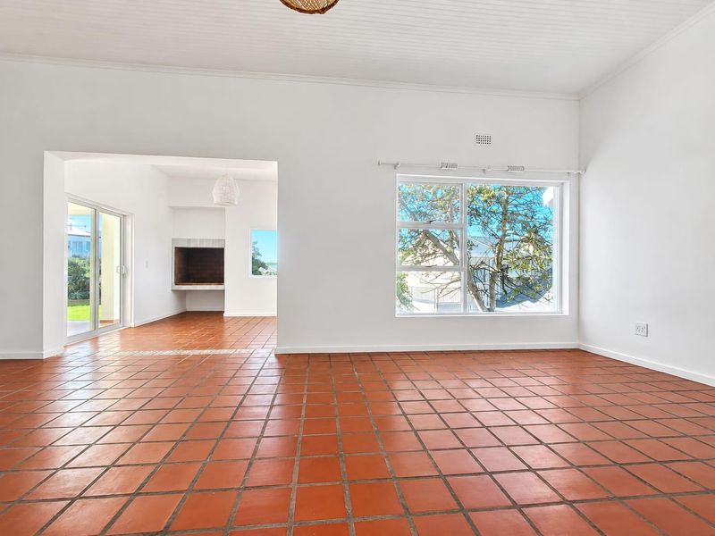 Spacious, light-filled living area featuring traditional terracotta tile flooring, a built-in fireplace, and large windows with access to an outdoor patio space.