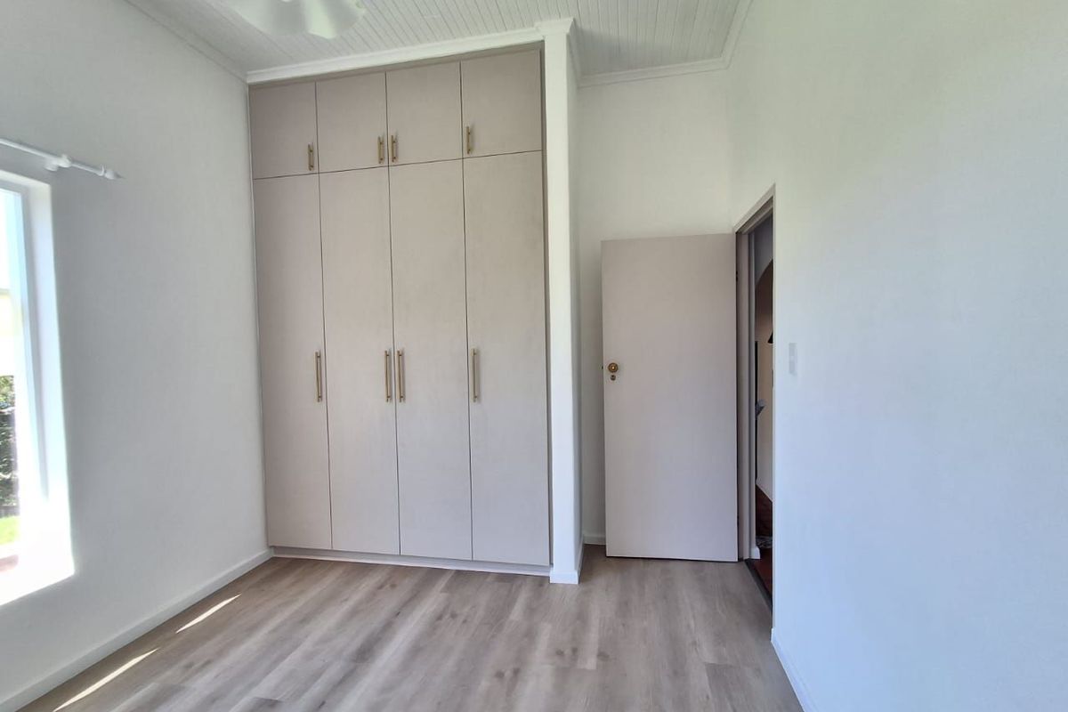 A bright, empty bedroom featuring modern built-in cupboards, light-toned laminate flooring, and a classic tongue and groove ceiling.