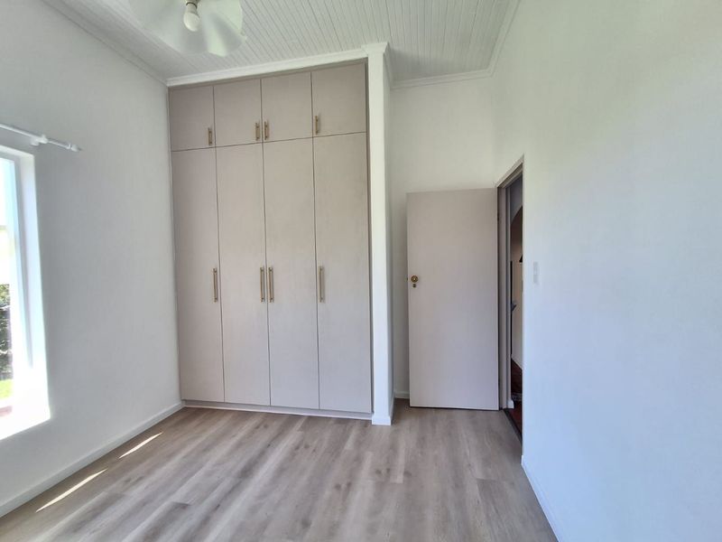 A bright, empty bedroom featuring modern built-in cupboards, light-toned laminate flooring, and a classic tongue and groove ceiling.