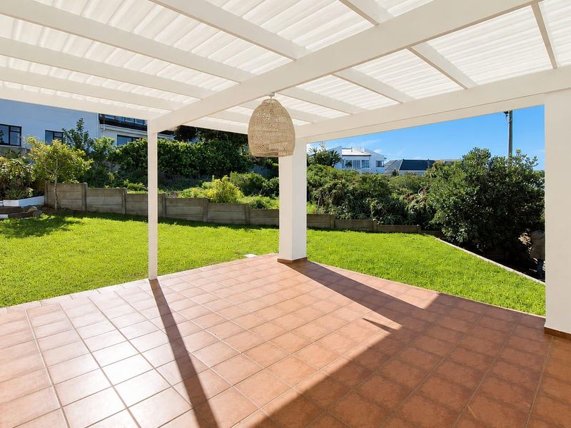 A spacious covered patio featuring tiled flooring and a pergola, overlooking a well-maintained garden with a retaining wall.
