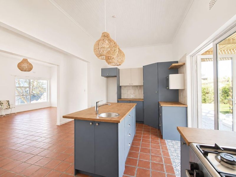 Bright open-plan kitchen featuring blue cabinetry, wooden countertops, a central island with sink, and direct access to the outdoor area through sliding doors.