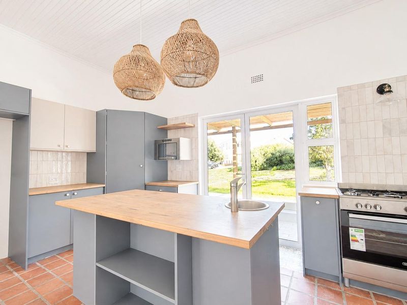 Modern kitchen featuring a central island with timber countertop, built-in oven, gas hob, and direct access to the garden through glass sliding doors.