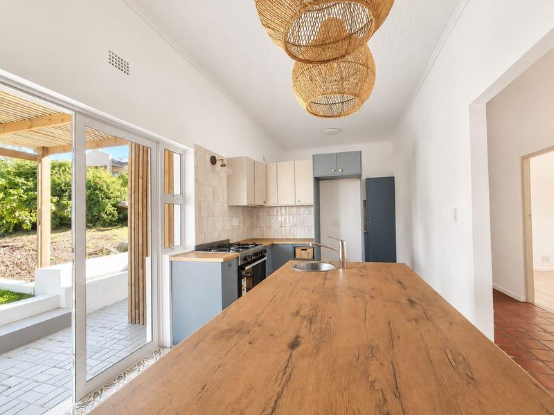Modern kitchen featuring a timber-topped island, built-in cabinetry, gas hob, and direct access to an outdoor patio area through sliding glass doors.