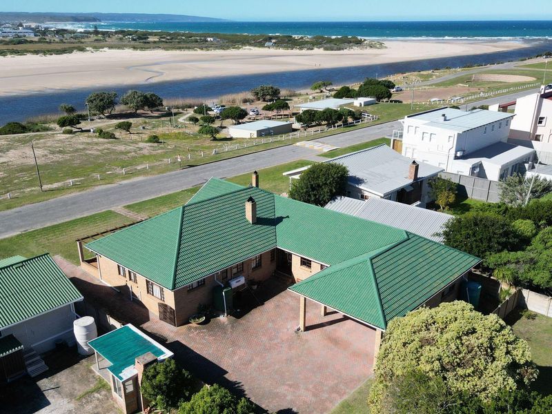 Aerial view of the property showcasing the green metal roof, paved driveway, carport, and proximity to the coastline and river estuary.