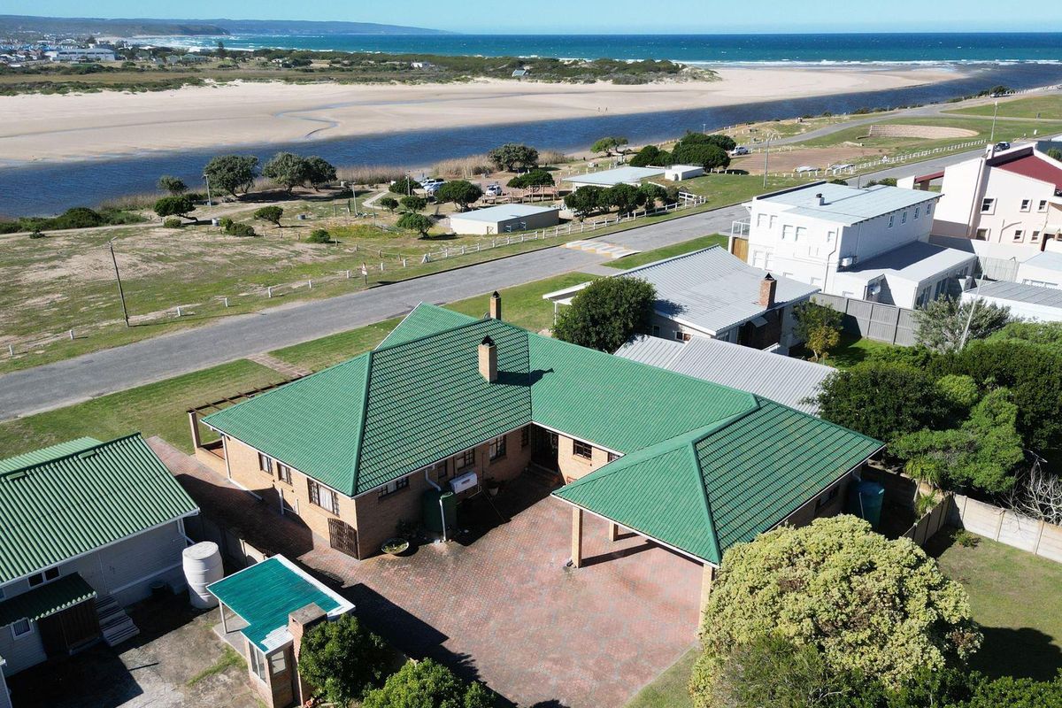 Aerial view of the property showcasing the green metal roof, paved driveway, carport, and proximity to the coastline and river estuary.