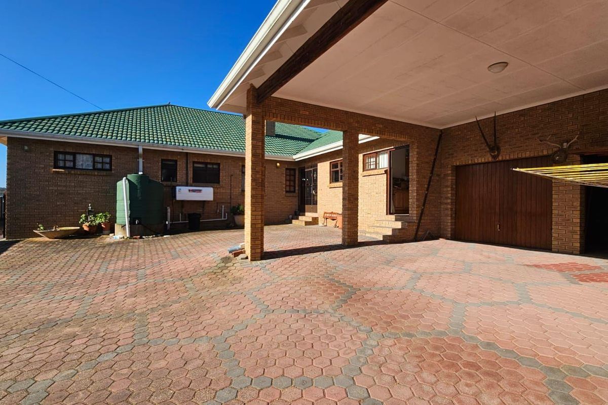 A spacious rear exterior area featuring a paved courtyard, covered patio space, brick facade, and a green tiled roof.