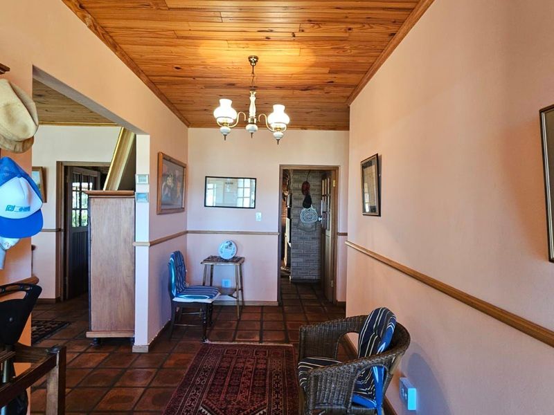 A spacious hallway featuring warm timber tongue and groove ceilings, terracotta floor tiles, and classic chair rail molding, connecting multiple areas of the home.