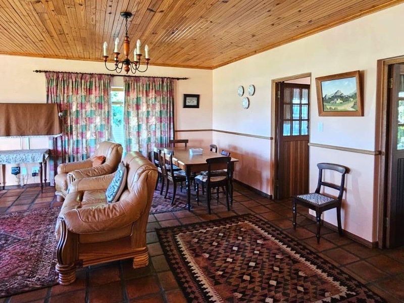 Spacious open-plan living and dining area featuring a rustic brick fireplace, exposed timber ceiling, and traditional terracotta floor tiles.