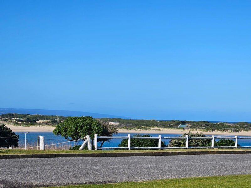 A scenic view overlooking a coastal landscape with a white timber fence and asphalt road in the foreground.