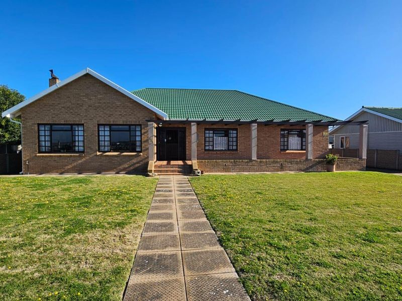 A well-maintained single-story brick house featuring a green metal roof, a covered front patio, and a paved walkway leading to the entrance.