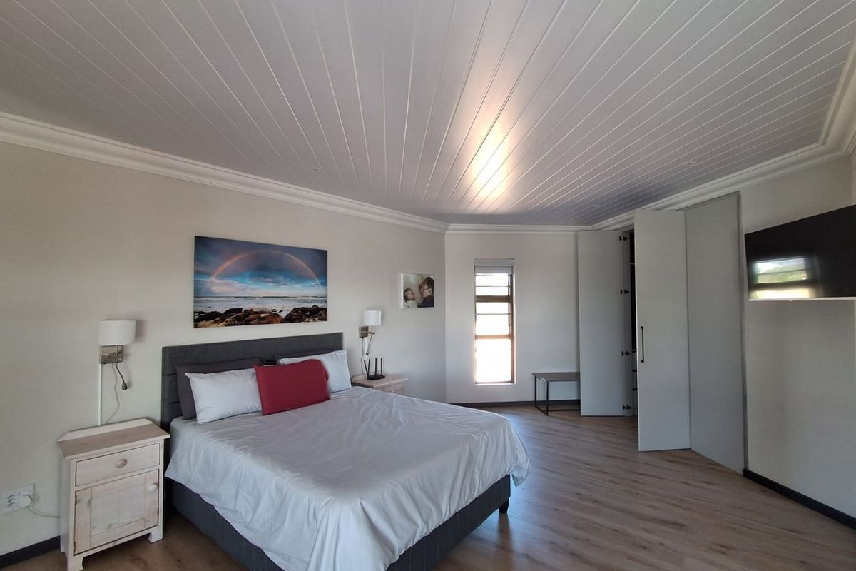 Spacious bedroom featuring light laminate flooring, a white tongue and groove ceiling with crown molding, and ample built-in cupboard storage.