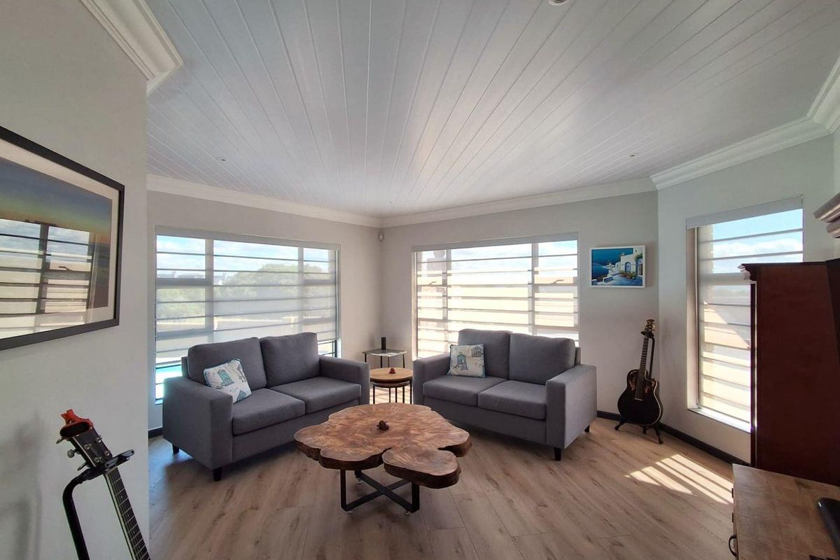 Bright and airy living room featuring timber-look flooring, a classic tongue and groove ceiling, and large windows that provide ample natural light.