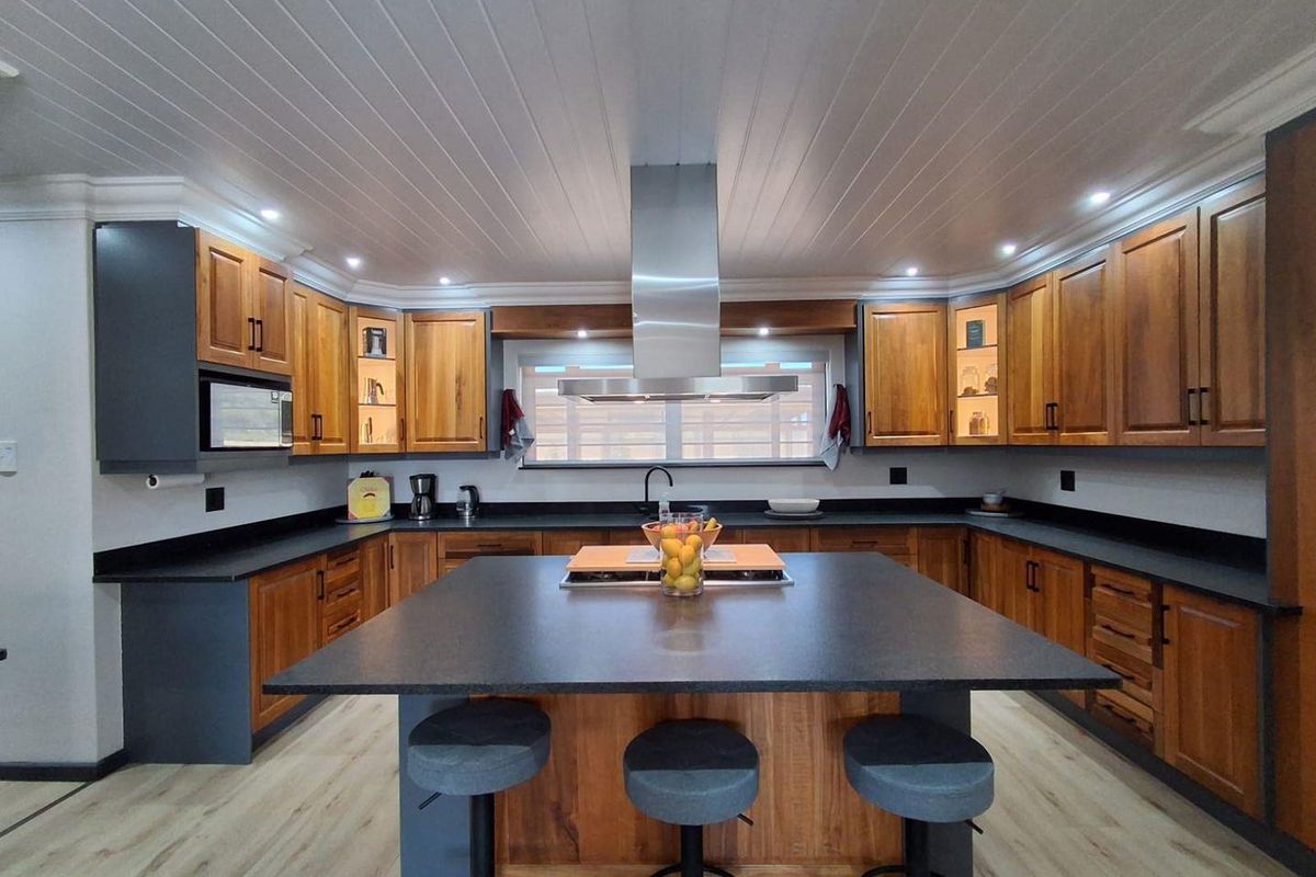 A modern, well-appointed kitchen featuring a large central island, extensive wooden cabinetry, stone countertops, and a sleek stainless steel extractor fan.