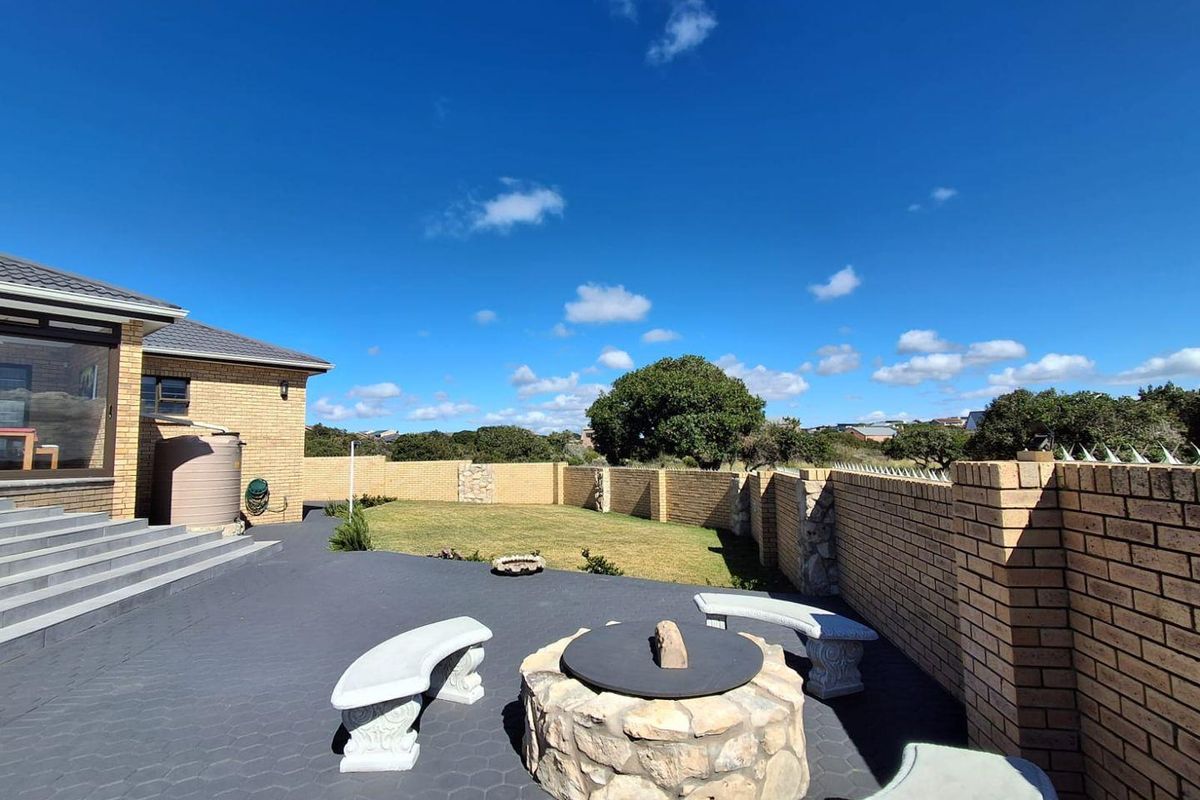 A well-maintained rear garden featuring a paved patio area, a stone fire pit, and a secure brick boundary wall.