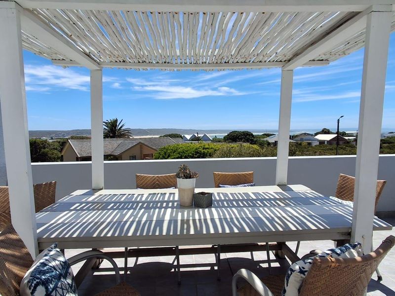 A covered outdoor patio featuring a white pergola structure and tiled flooring, offering scenic coastal views.