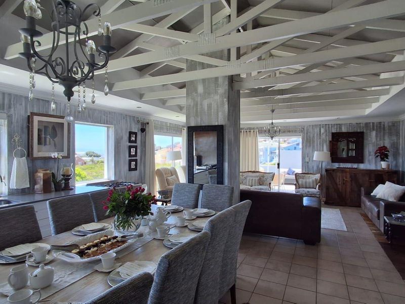 Spacious open-plan living and dining area featuring exposed timber ceiling beams, tiled flooring, and large windows with natural light.