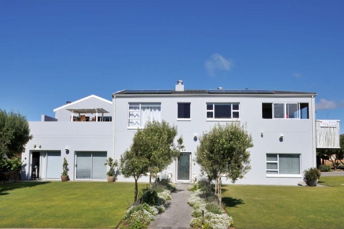 A well-maintained two-story residential property featuring a landscaped garden, paved walkway, solar panels, and an upper-level balcony.