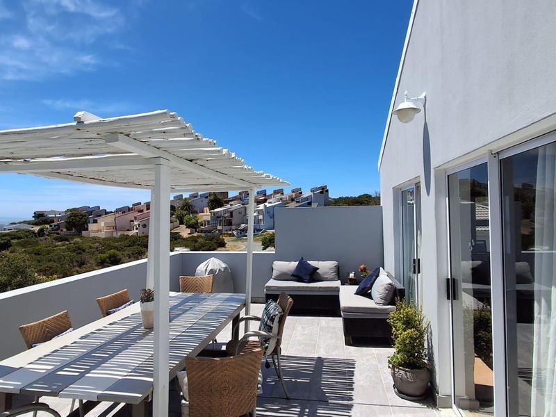 A spacious outdoor balcony featuring a white pergola, tiled flooring, and sliding glass door access, offering a pleasant area for outdoor living.