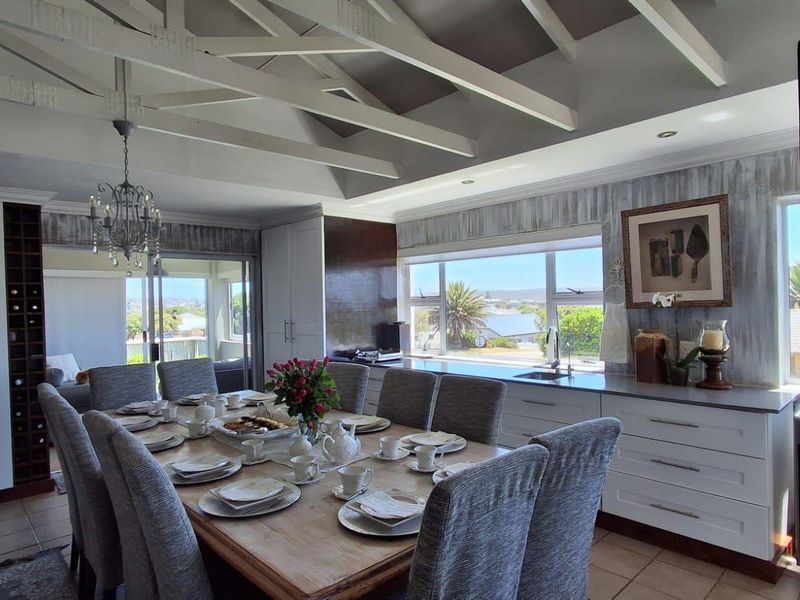 Spacious open-plan dining and kitchen area featuring exposed timber ceiling beams, ample built-in cabinetry, and large windows with scenic views.