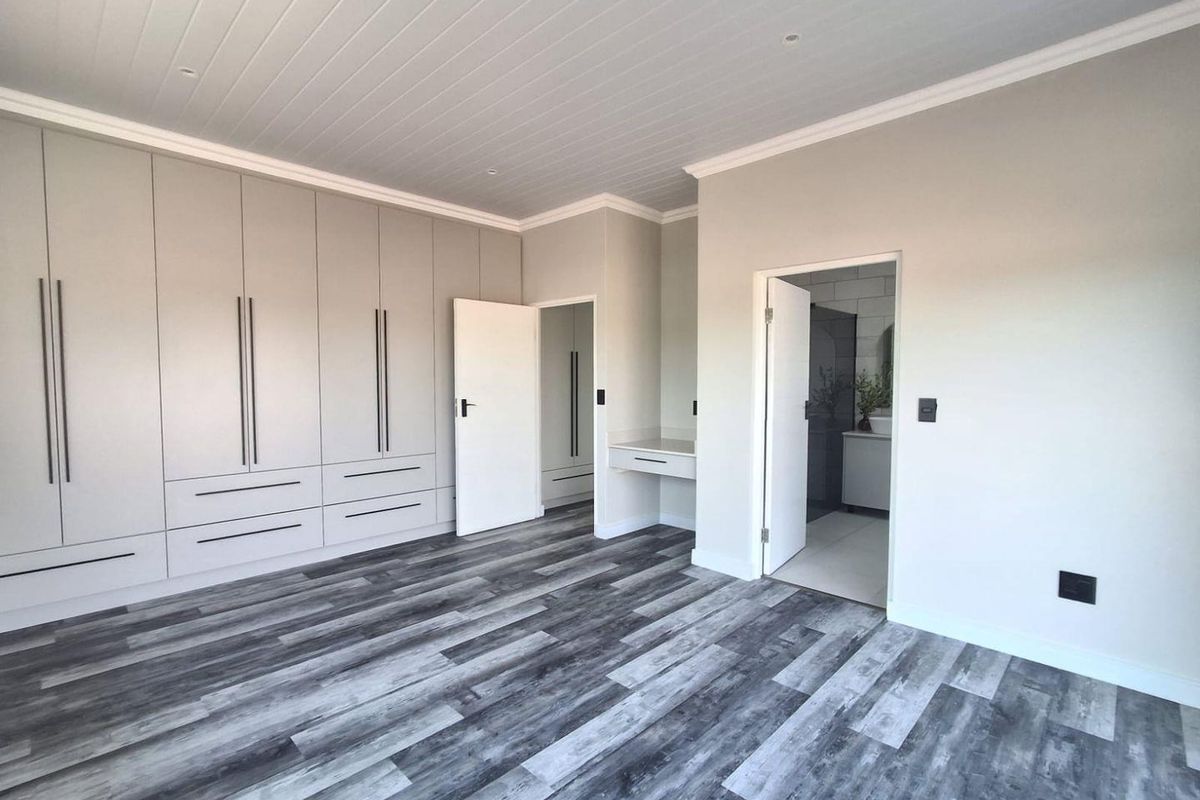 Spacious bedroom featuring modern grey laminate flooring, extensive built-in cabinetry, a dedicated vanity area, and direct access to an en-suite bathroom.