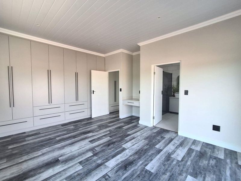 Spacious bedroom featuring modern grey laminate flooring, extensive built-in cabinetry, a dedicated vanity area, and direct access to an en-suite bathroom.